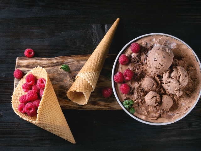Шарики шоколадного мороженого на столе с вафельными рожками и малиной