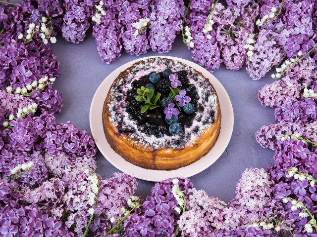 Аппетитный пирог с ягодами на столе с цветами сирени