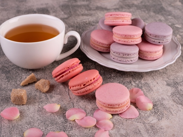 Сладкий десерт макарун на столе с чашкой чая, сахаром и лепестками розы