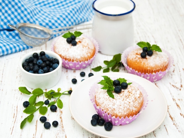 Кексы с сахарной пудрой на столе с молоком и черникой