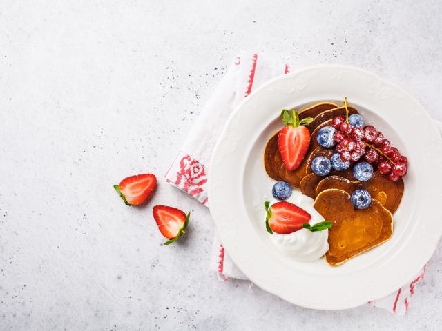 Оладьи со сметаной в тарелке с ягодами черники, клубники и красной смородины