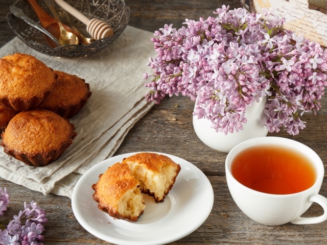 Сладкие кексы на столе с чаем и букетом сирени