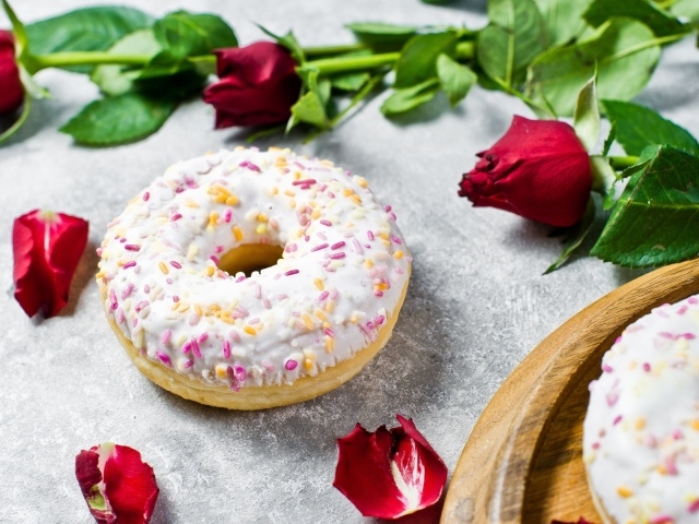 Сладкий пончик с глазурью на столе с красными розами