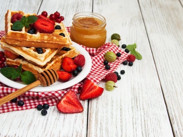 Сладкие вафли на столе с ягодами и медом