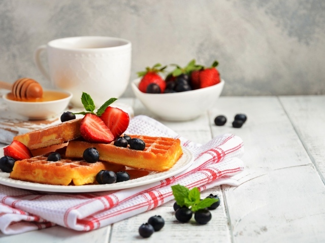 Сладкие вафли с ягодами черники и клубники на столе с медом и чаем