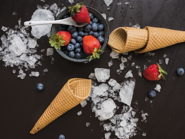 Вафельные рожки на столе со льдом и ягодами черники и клубники