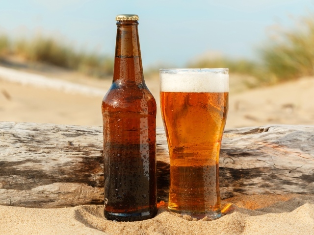 Бутылка пива и бокал стоят на песке 