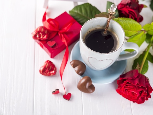 Чашка кофе на столе с шоколадными конфетами, подарком и красной розой
