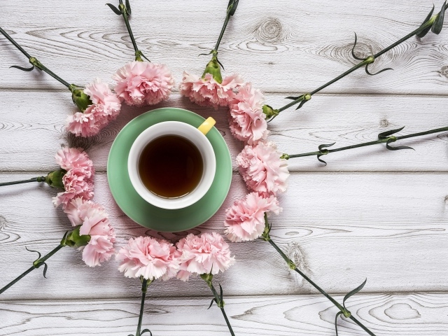 Чашка чая с розовыми гвоздиками на деревянном фоне