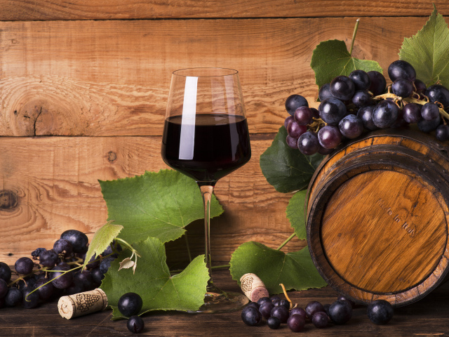 Бокал красного вина  на столе с виноградом и бочкой