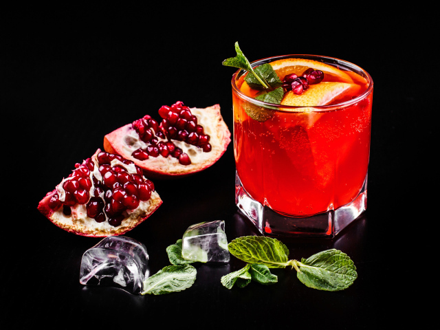 Алкогольный напиток в стакане на черном фоне с гранатом, кусочками льда и мятой