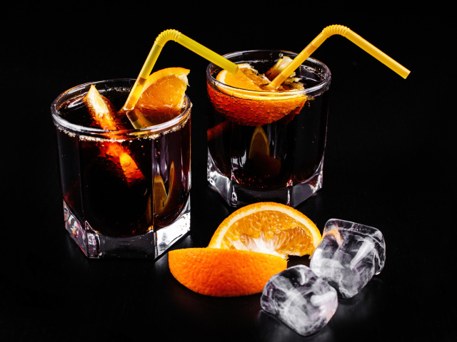 Коктейль с кусочками апельсина на черном фоне со льдом