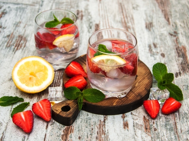 Холодный мохито на столе с ягодами клубники, лимоном и мятой