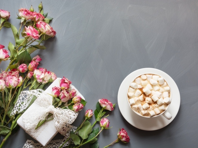 Чашка кофе с маршмеллоу на столе с подарком и букетом роз