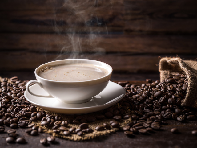 Чашка горячего ароматного кофе на столе с зернами