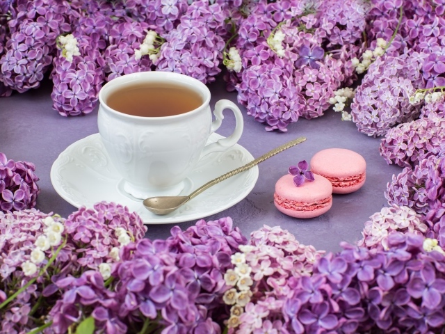 Чашка чая на столе с цветами сирени и десертом макарон