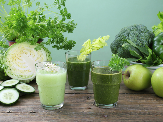 Зеленый овощной смузи в стаканах на столе со свежими овощами и яблоками