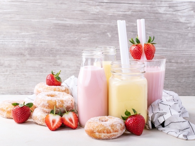 Молочные коктейли на столе с пончиками и ягодами клубники 