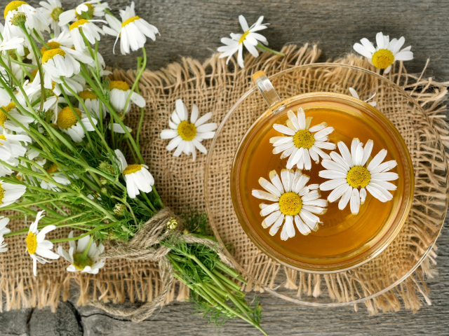 Чай в стеклянной чашке на столе с ромашкой