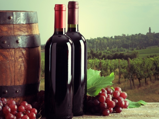 Две бутылки красного вина на столе с виноградом и бочкой