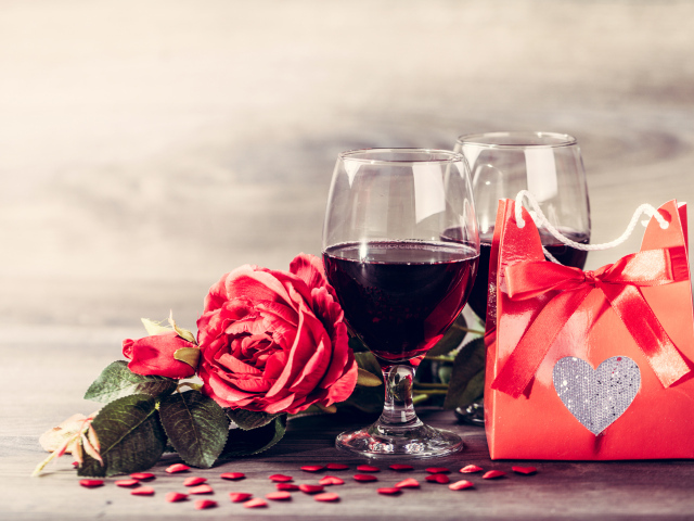 Два бокала красного вина на столе с розой и подарком 