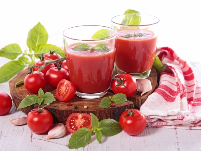 Два стакана томатного сока на столе с помидорами и зеленью 