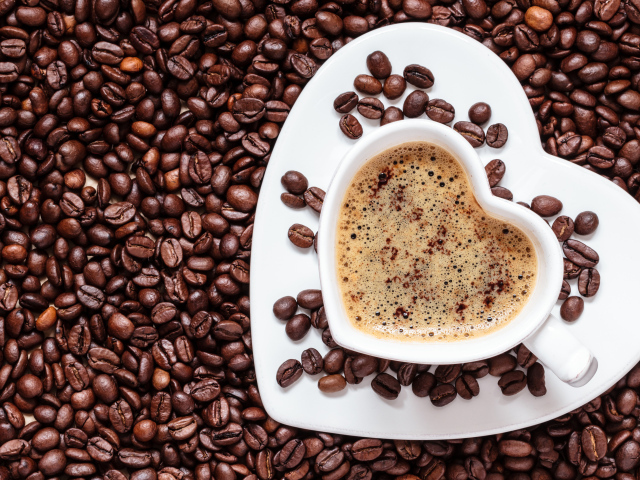 Белая чашка в форме сердца стоит на кофейных зернах 