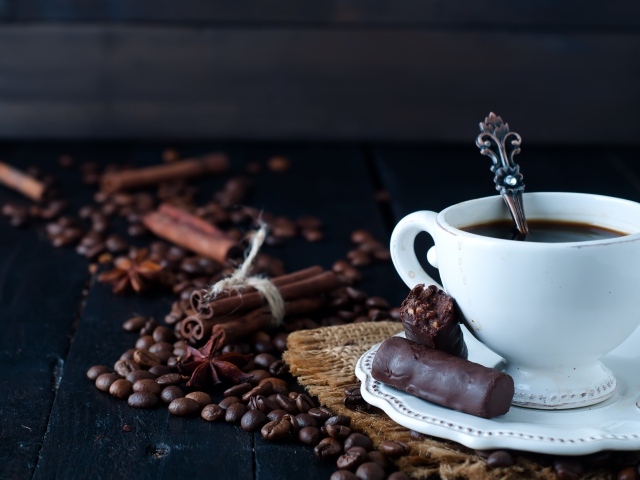Белая чашка кофе на столе с конфетами, корицей, бадьяном и зернами