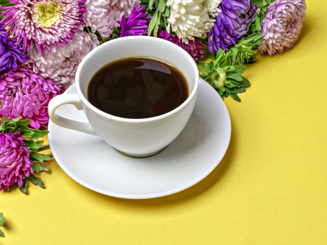 Белая чашка кофе на желтом фоне с букетом цветов астры