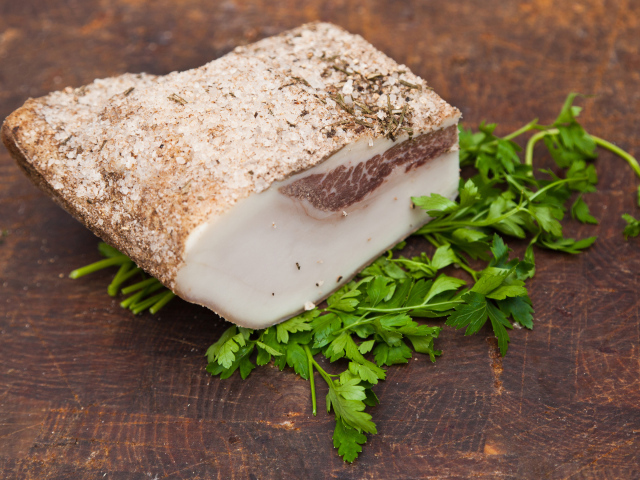 Кусок сала со специями на столе с зеленью петрушки