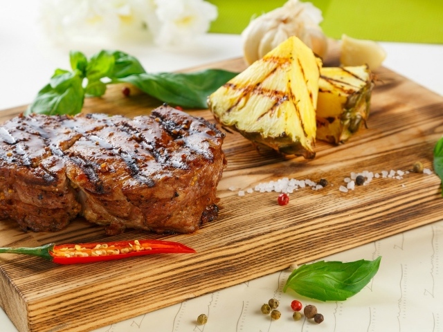 Кусок мяса гриль на деревянной доске с кусочками ананаса и базиликом