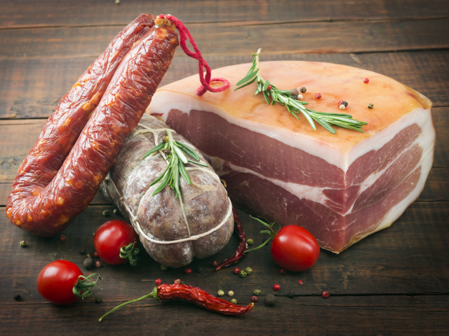 Кусок мяса и колбаса на деревянном столе с помидорами и специями