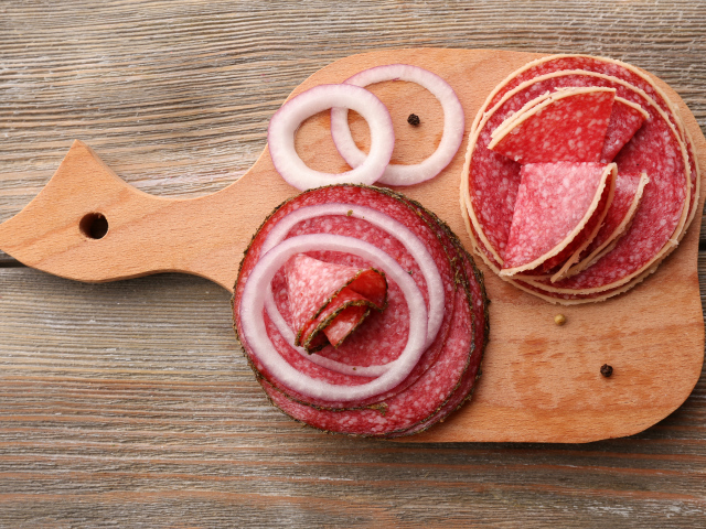 Аппетитные кусочки колбасы на разделочной доске с кольцами лука