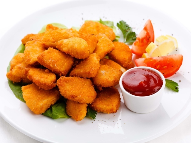 Куриные наггетсы с соусом и помидорами на белой тарелке 