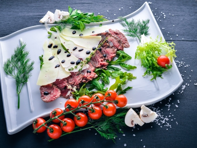 Мясо с сыром, овощами и зеленью на тарелке