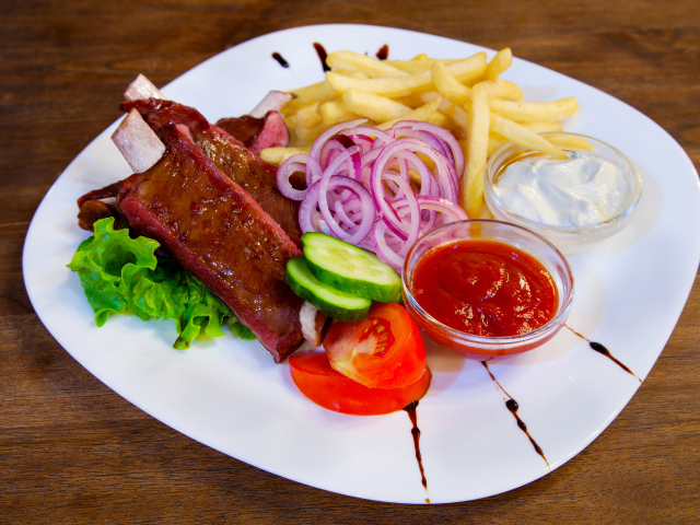 Мясо с овощами и картофелем фри на большой белой тарелке с соусом