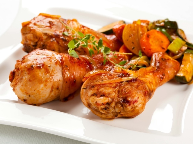 Жареные куриные ножки с овощами на белом фоне