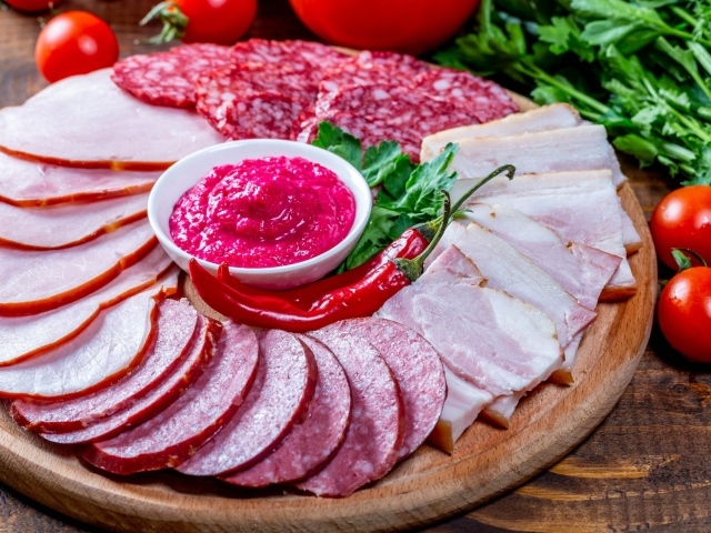 Мясная нарезка на доске с соусом, красным перцем,  помидорами и зеленью 