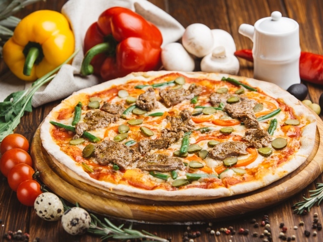 Свежая пицца с мясом и огурцами на столе с овощами
