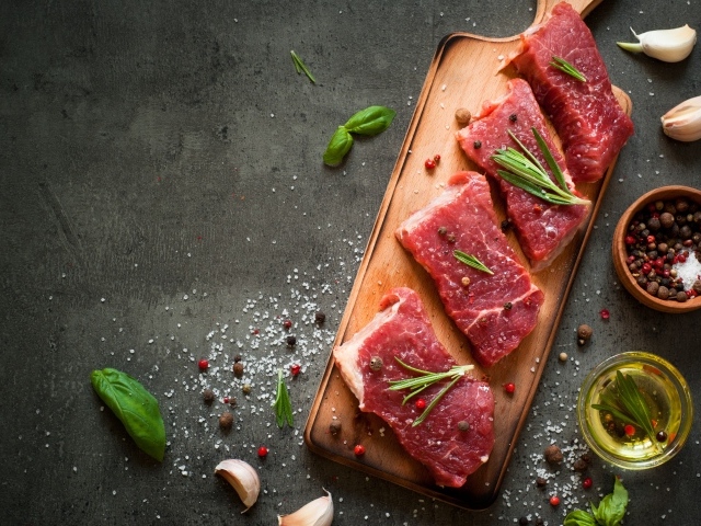 Куски мяса на разделочной доске с зеленью и специями