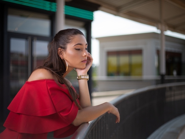 Задуманная девушка в красном платье стоит у перил 