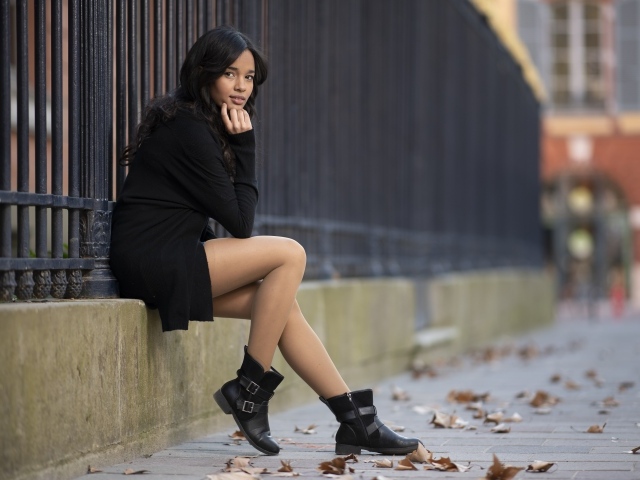 Молодая девушка в черном сидит у железного забора