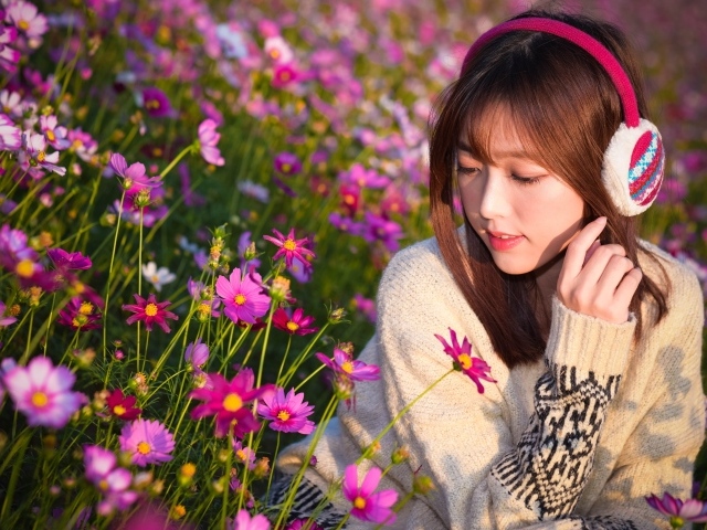 Девушка азиатка в наушниках сидит в цветах космеи