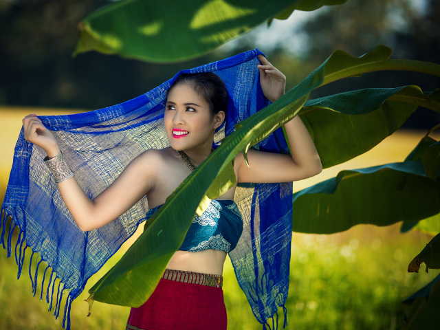 Красивая девушка азиатка с синим палантином у зеленых листьев