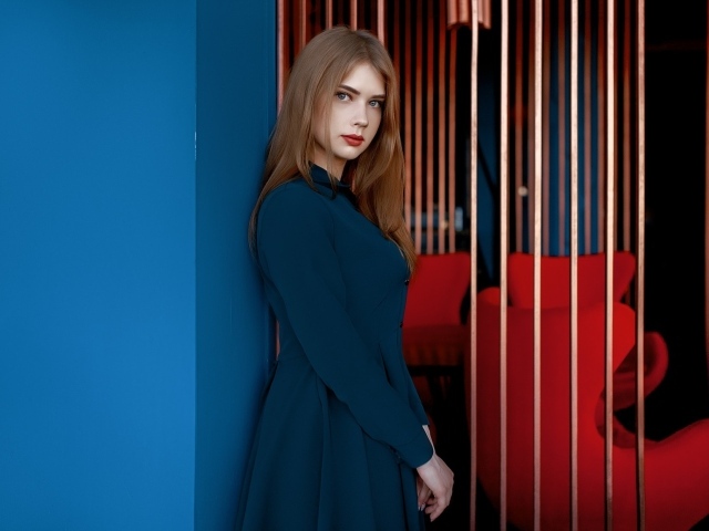 Красивая голубоглазая девушка стоит в пальто у стены