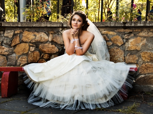 Красивая невеста в белом платье сидит на лавке