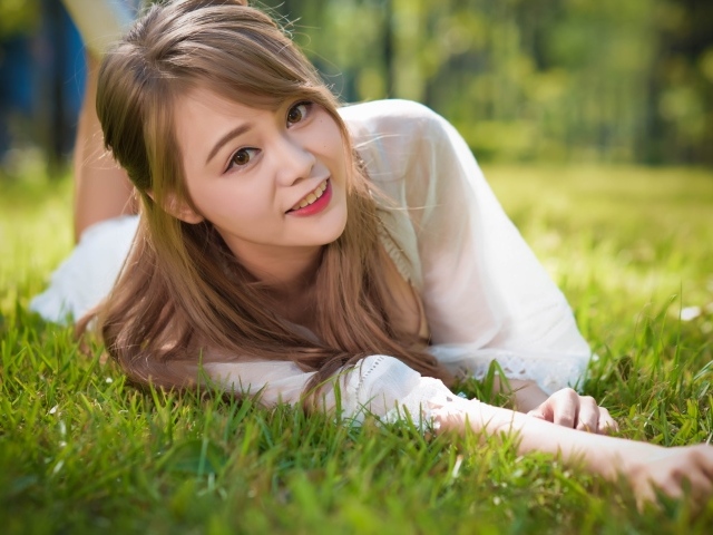 Красивая кареглазая девушка азиатка лежит на зеленой траве