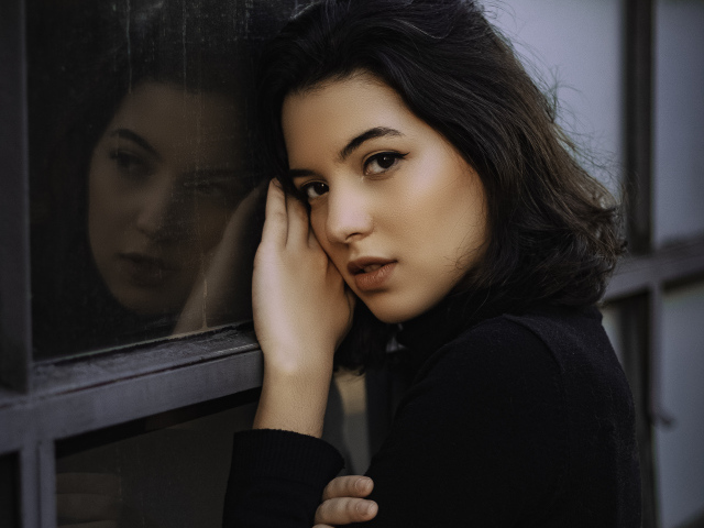 Красивая кареглазая девушка стоит у окна