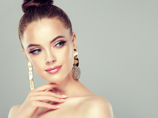 Красивая девушка шатенка с золотыми серьгами в ушах на сером фоне