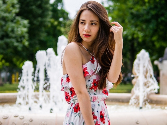 Красивая шатенка в цветастом платье у фонтана летом